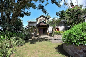 A stone house with a stone staircase leading to the entrance, surrounded by lush greenery and trees.