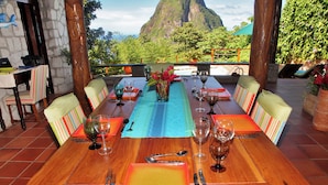 A dining table set for six with a view of a mountain and lush greenery. - Private Pool Villa with Iconic Piton Views (Soufrière)