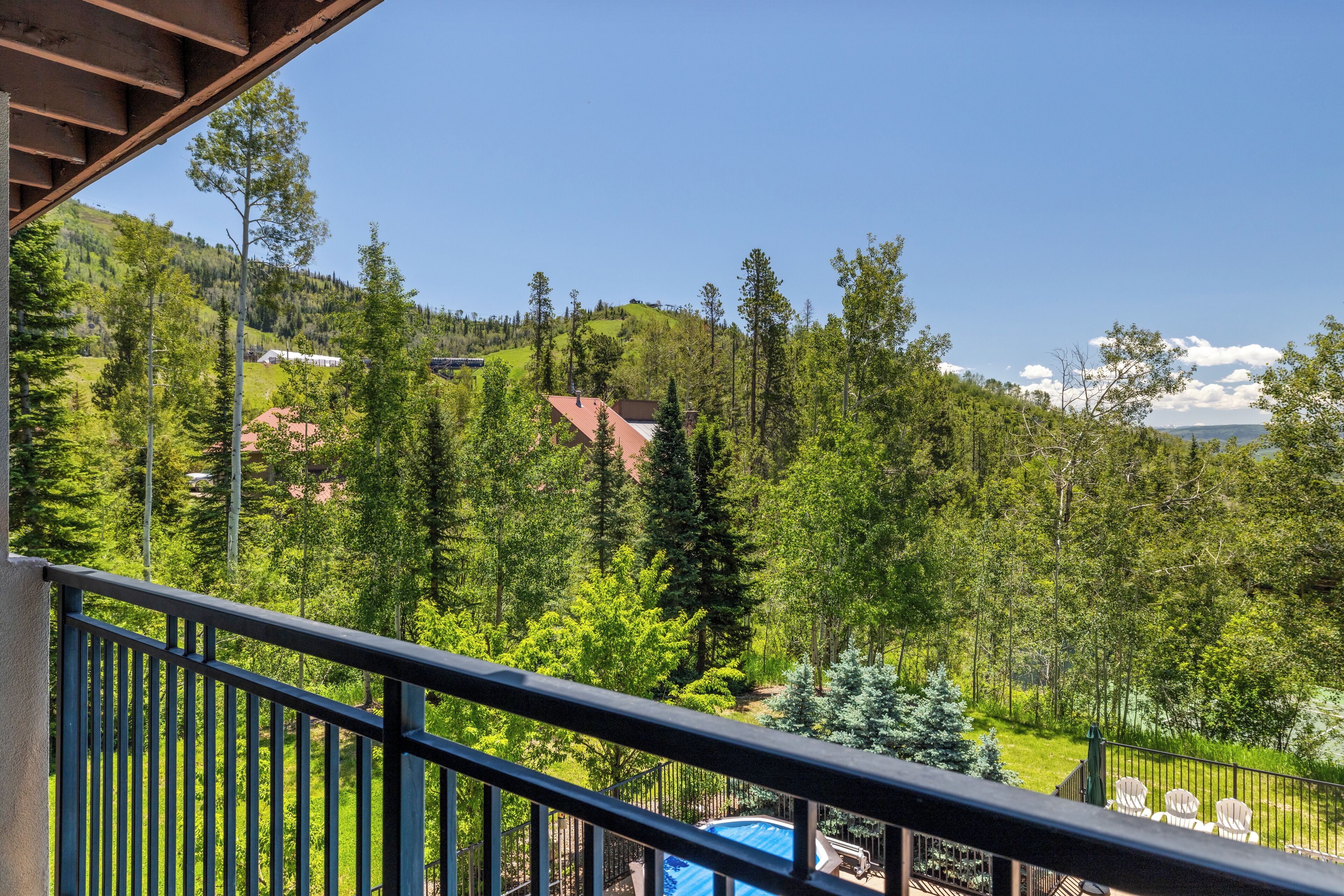 A balcony with a view of a mountainous landscape, trees, and a swimming pool.