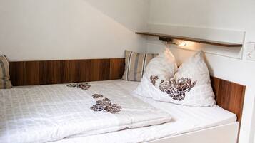 A bed with a wooden headboard, two pillows with floral patterns, and a bedside shelf with a light.