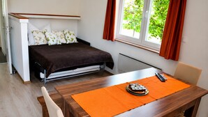 A bedroom with a bed, a small table with a remote control, and a window with curtains. - Panorama Apartment on Lake Ossiach (Steindorf am Ossiacher See)