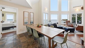 Ett rymligt vardagsrum med ett stort matbord, bekväma sittplatser och utsikt över havet.