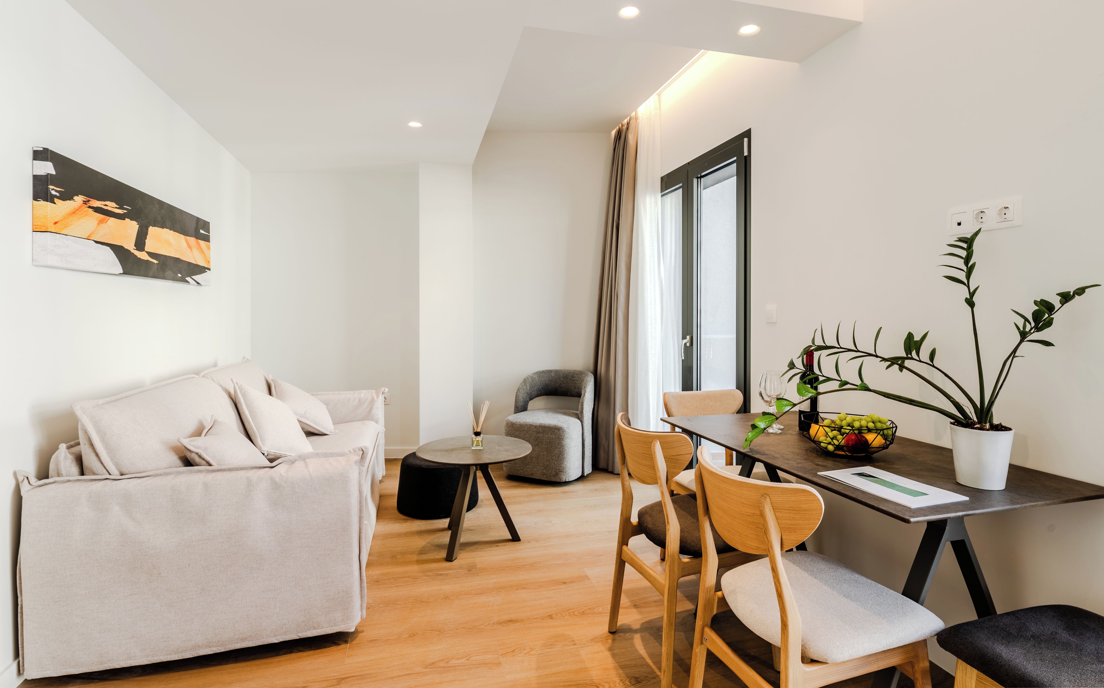 Un salon moderne avec un canapé, une table à manger et des chaises, une petite table ronde avec une bougie et une plante en pot.