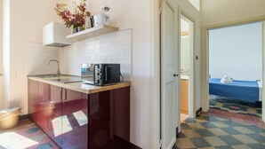A compact kitchen with a microwave, toaster, and a small shelf with decorative items. - One Bedroom Apartment (ROMA)
