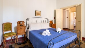 A bedroom with a bed, a wooden chair, a nightstand, and a picture on the wall. - One Bedroom Apartment (ROMA)