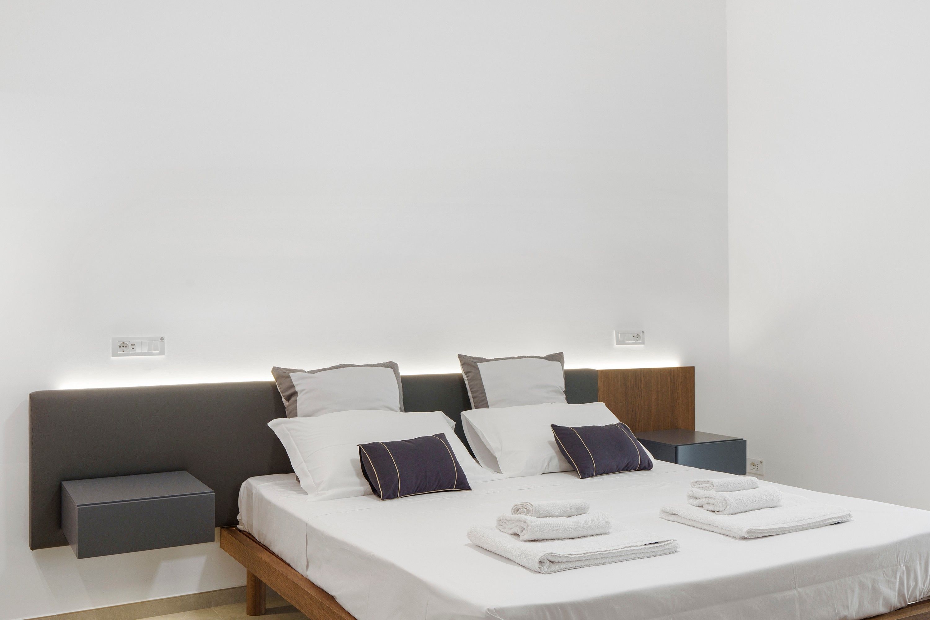 A modern hotel room with a neatly made bed, bedside tables, and a wall-mounted light fixture.
