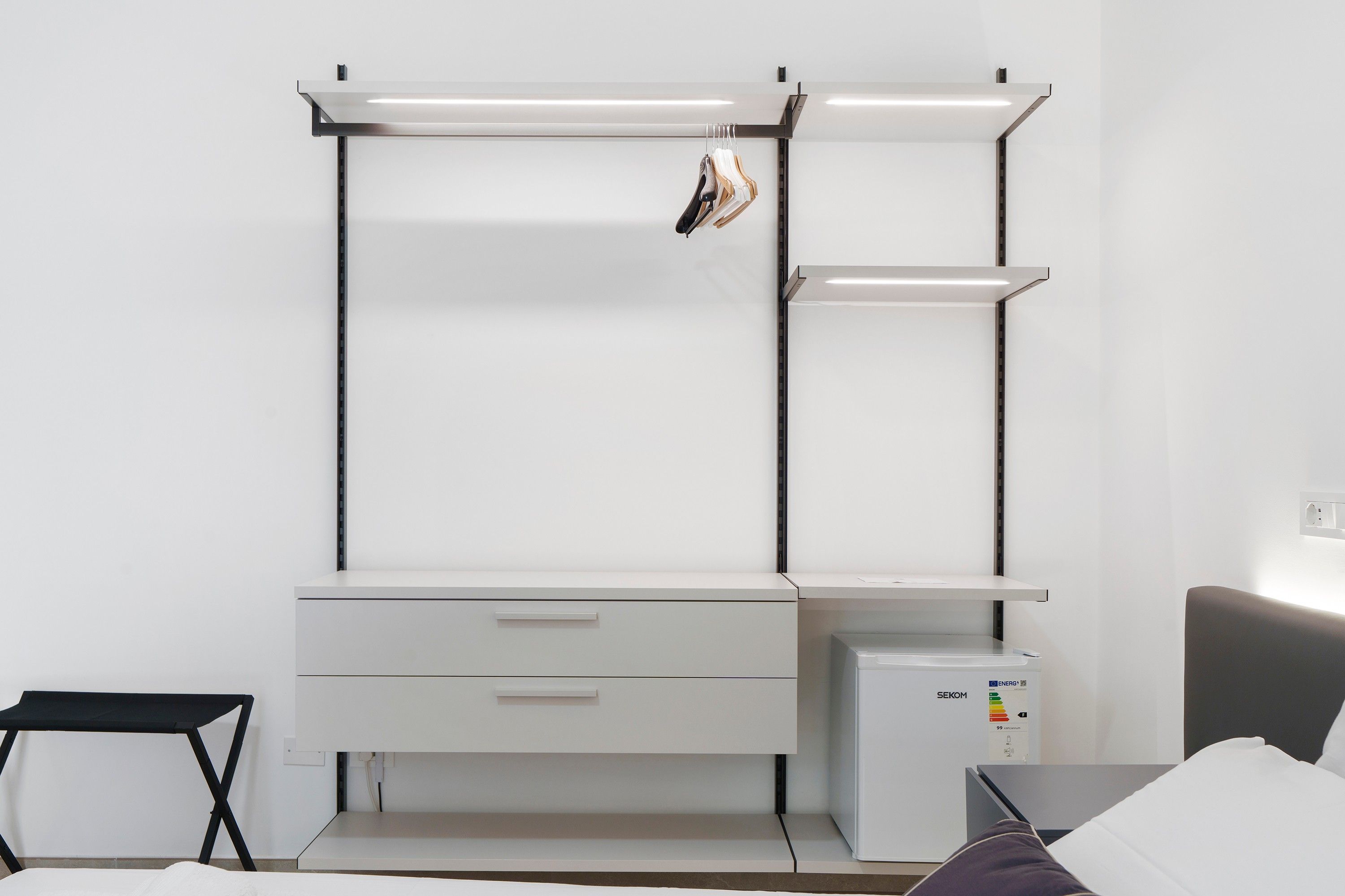Una habitación minimalista con un escritorio blanco, un mueble pequeño y una cama.