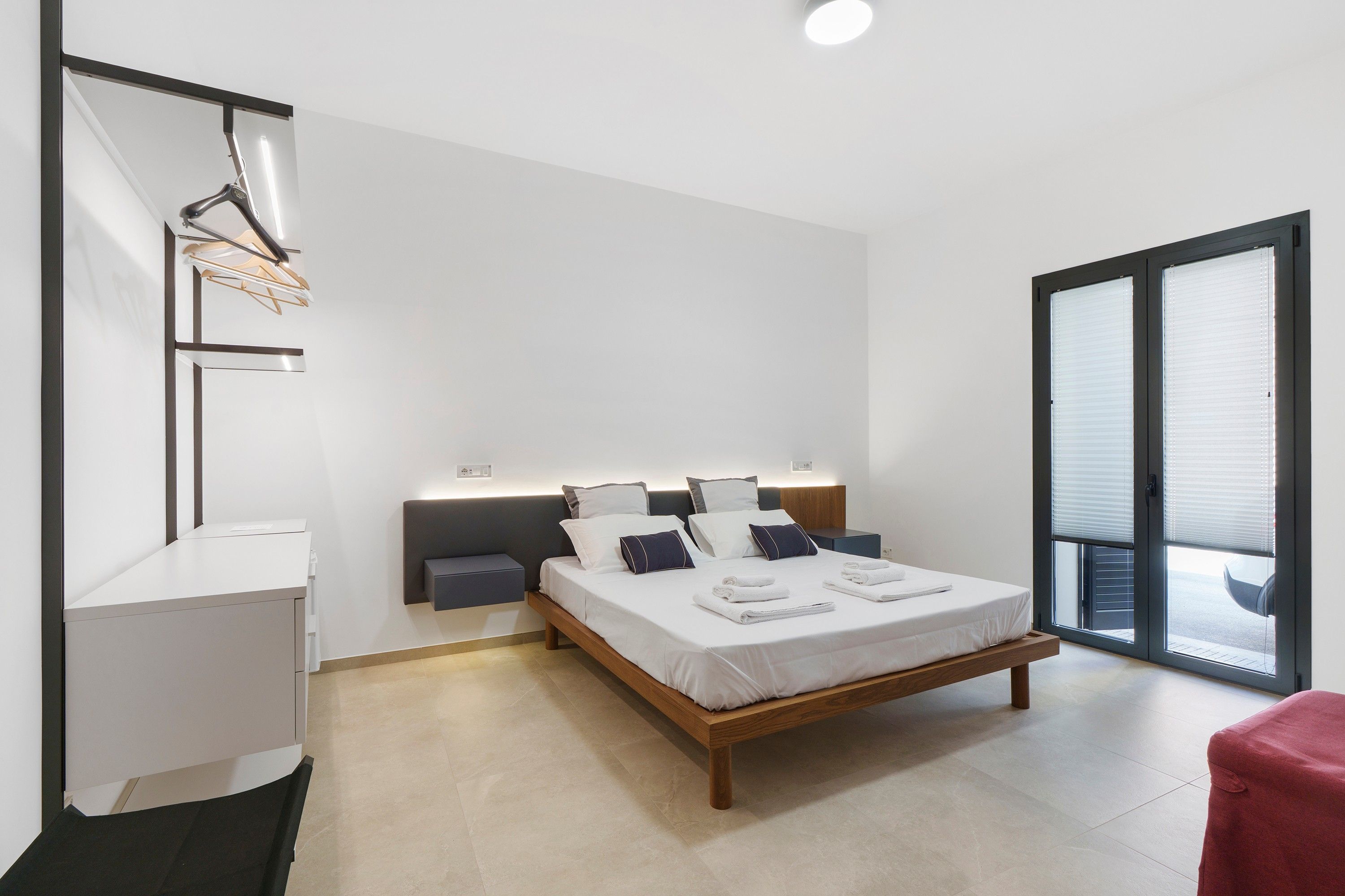 Una camera da letto moderna con un letto, comodini, una scrivania e una porta scorrevole in vetro che dà sull'esterno.
