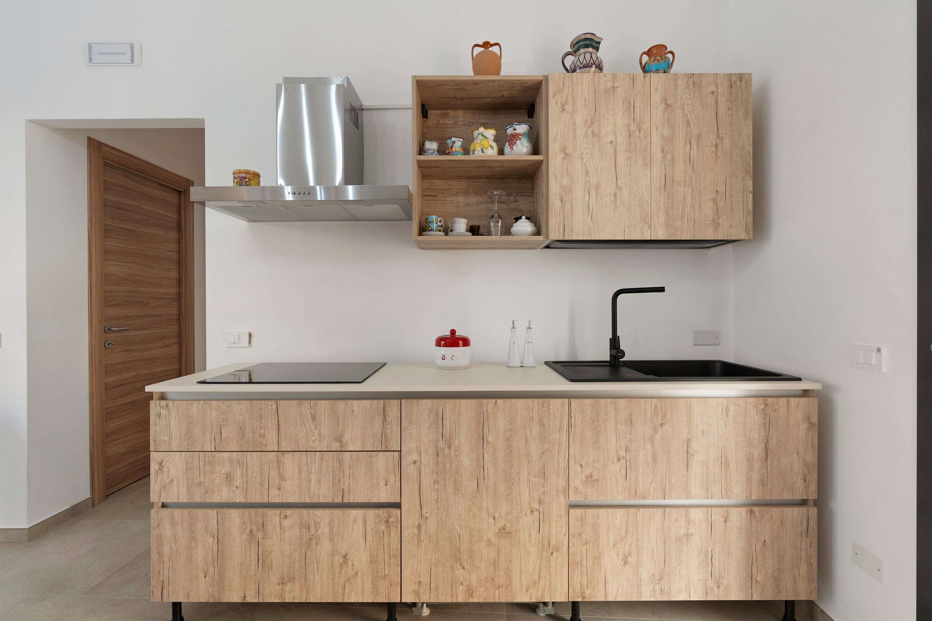 Una cocina con un mueble de madera, una campana extractora de acero inoxidable, un lavamanos doble y una puerta de madera.