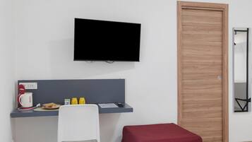 Une pièce dotée d’un téléviseur à écran plat fixé au mur, d’un bureau avec une chaise, d’un coussin rouge et d’une porte en bois.
