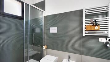 Une salle de bain moderne avec une douche à parois de verre, des toilettes blanches, un lavabo et un porte-serviettes muni d’un panier.