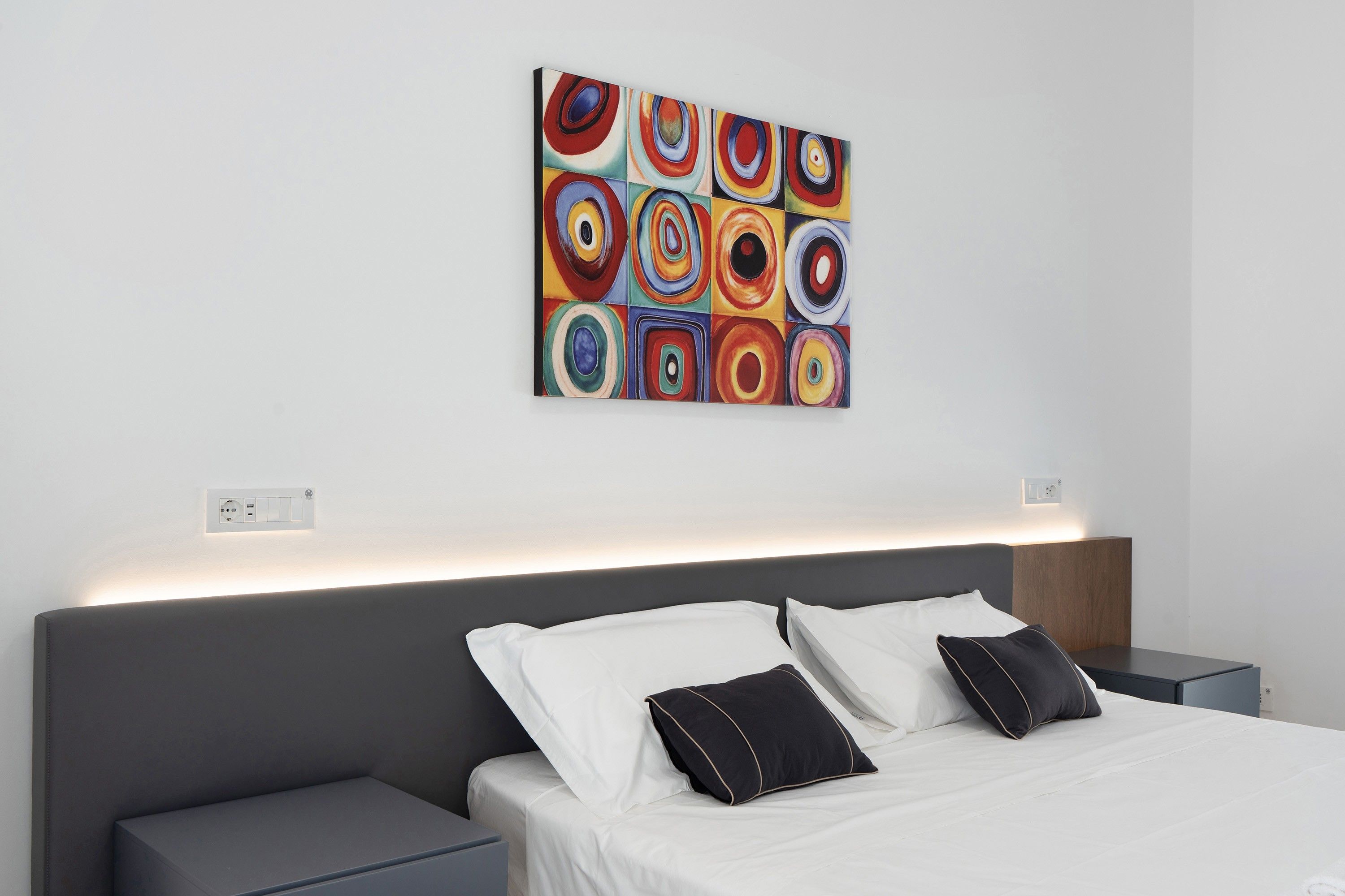 Een moderne hotelkamer met een net opgemaakt bed, een nachtkastje en een wanddecoratie.