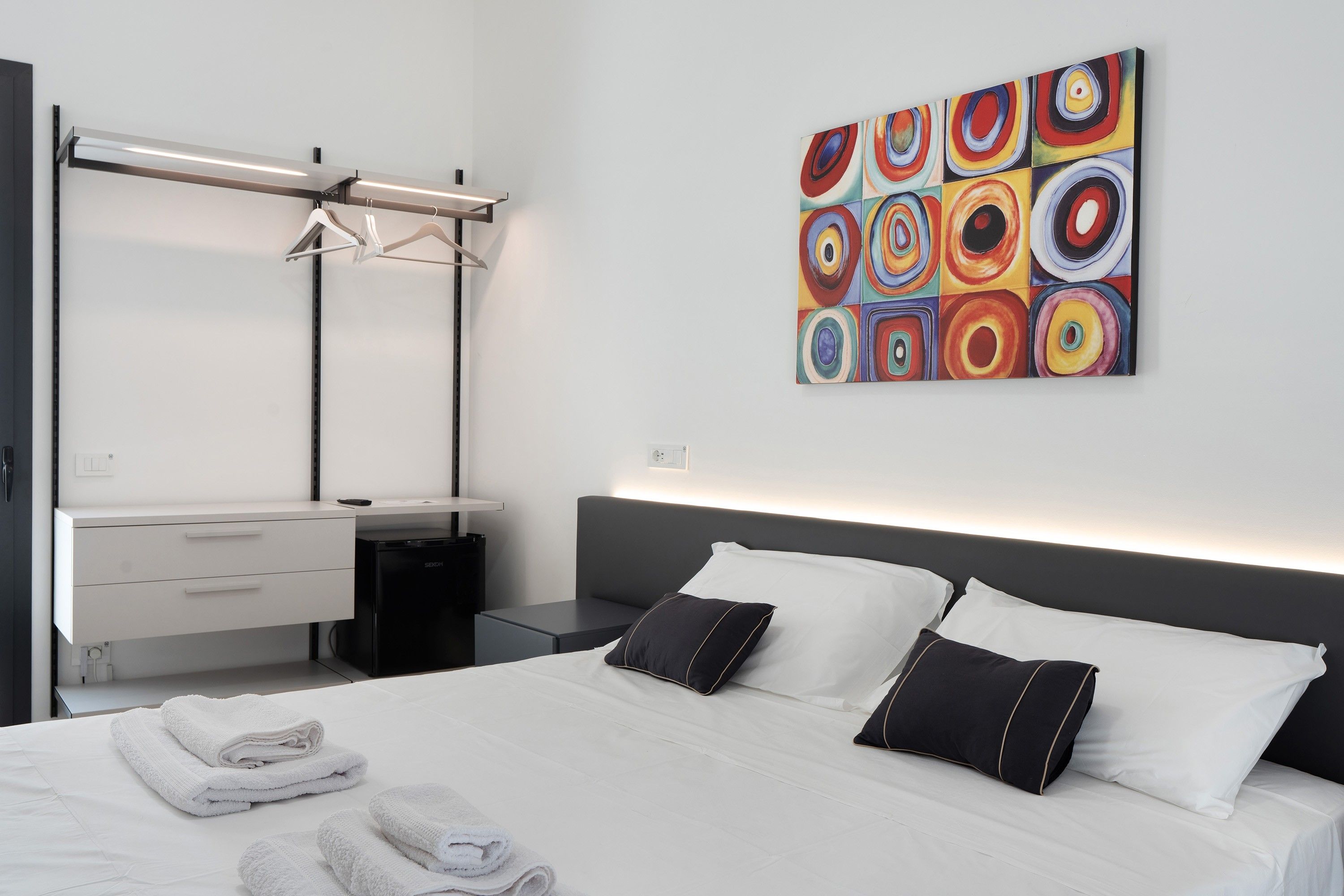 Una habitación de hotel moderna con una cama, una mesita de noche, una obra de arte en la pared y un armario.