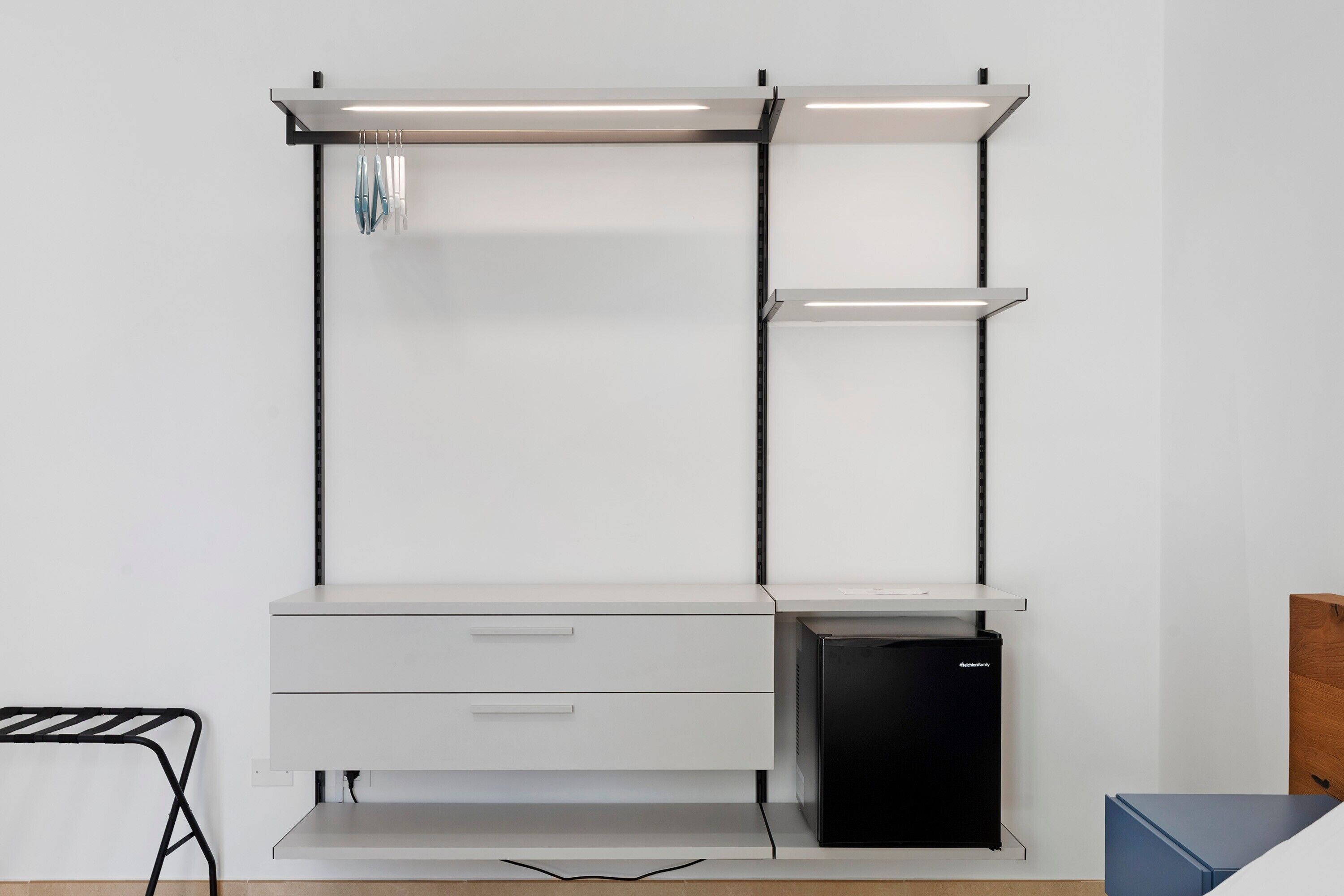 A white desk with a black computer, a drawer, and a shelf with a black object on it.