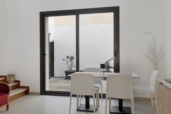 Un comedor con una mesa y sillas, un ventanal corredero que da al exterior y una planta en maceta.