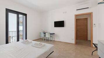 Une chambre d’hôtel comprenant un lit, un bureau avec une chaise, une télévision et une porte donnant sur une autre pièce.