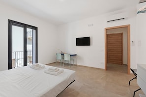 Una habitación de hotel con cama, escritorio y silla, televisor y puerta que da a otra habitación.