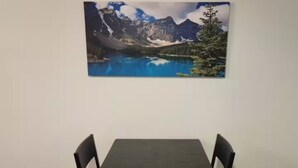 Un'area pranzo con tavolo e sedie, un dipinto che raffigura un paesaggio montano sulla parete e pavimento in legno.