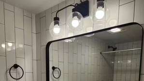 Un bagno con parete rivestita in piastrelle bianche, un lavabo rettangolare con rubinetteria nera e uno specchio grande con cornice nera.