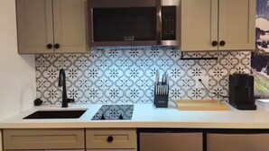 Una cucina con mobili beige, un forno a microonde in acciaio inossidabile, un lavello e una lavastoviglie.