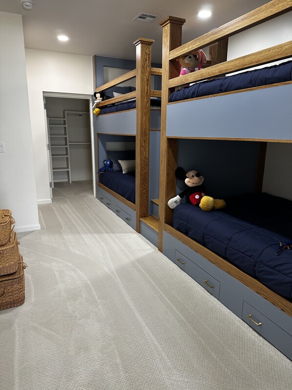 Habitación con literas de madera, un armario con escalera y suelo alfombrado.