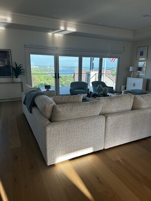 Un salon comprenant un grand canapé, une table basse et donnant sur l’extérieur grâce à une porte-fenêtre coulissante.
