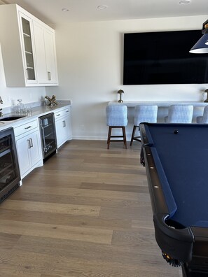 Una cocina moderna con armarios blancos, un enfriador de vinos empotrado y una mesa de billar.