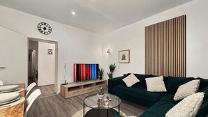 Una sala de estar moderna con un sofá verde oscuro, una mesa redonda de centro, un televisor de pantalla plana y un revestimiento de pared de madera.