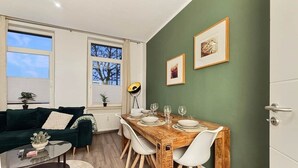 Una sala moderna con pared verde, una mesa de comedor de madera dispuesta para cuatro comensales, un sofá verde oscuro y una pequeña mesa de centro.