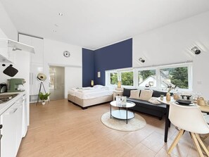 Een moderne woonkamer met een bed, bank, eettafel en keuken.