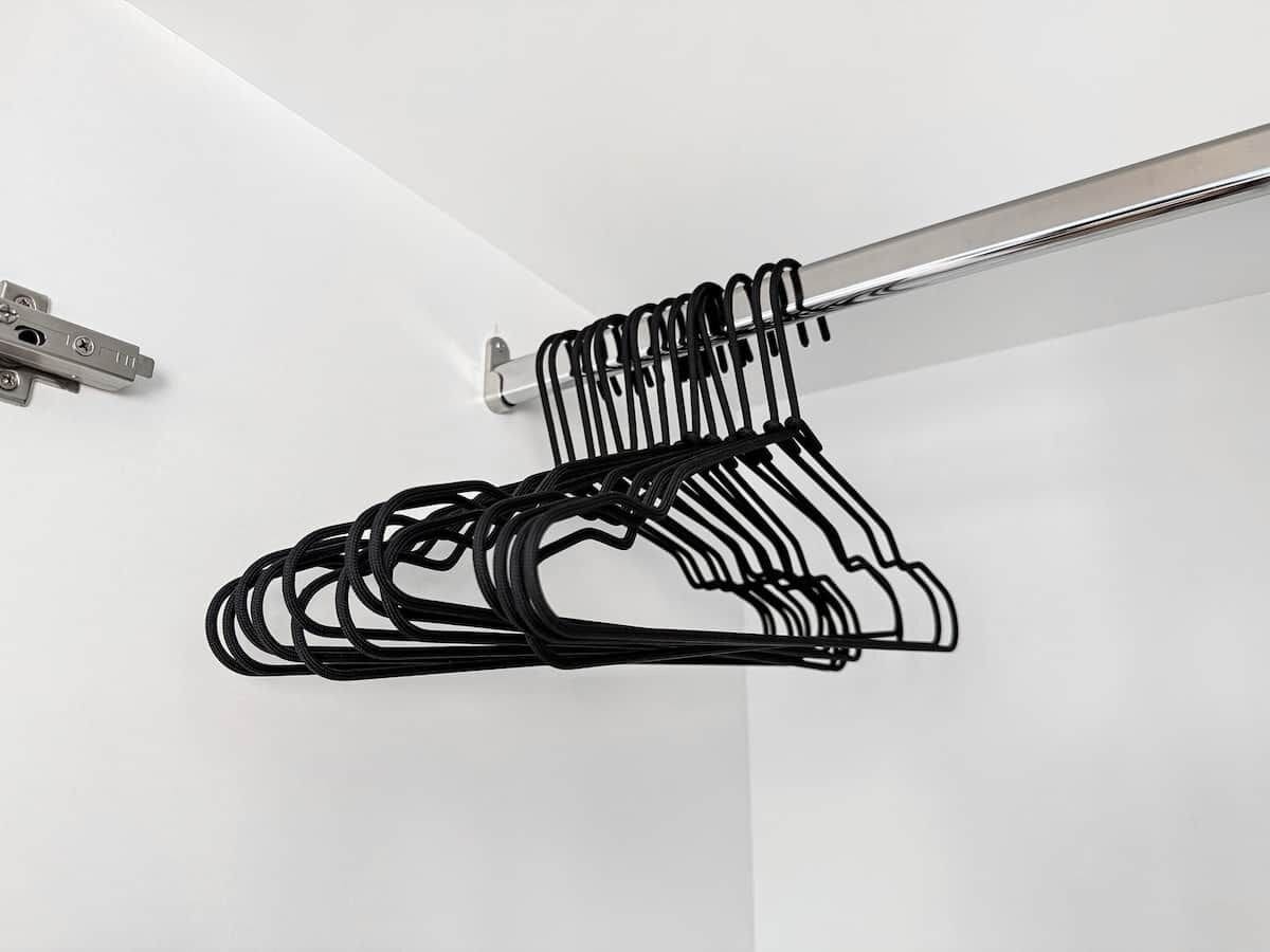A metal hanger rack with multiple black hangers against a white wall.