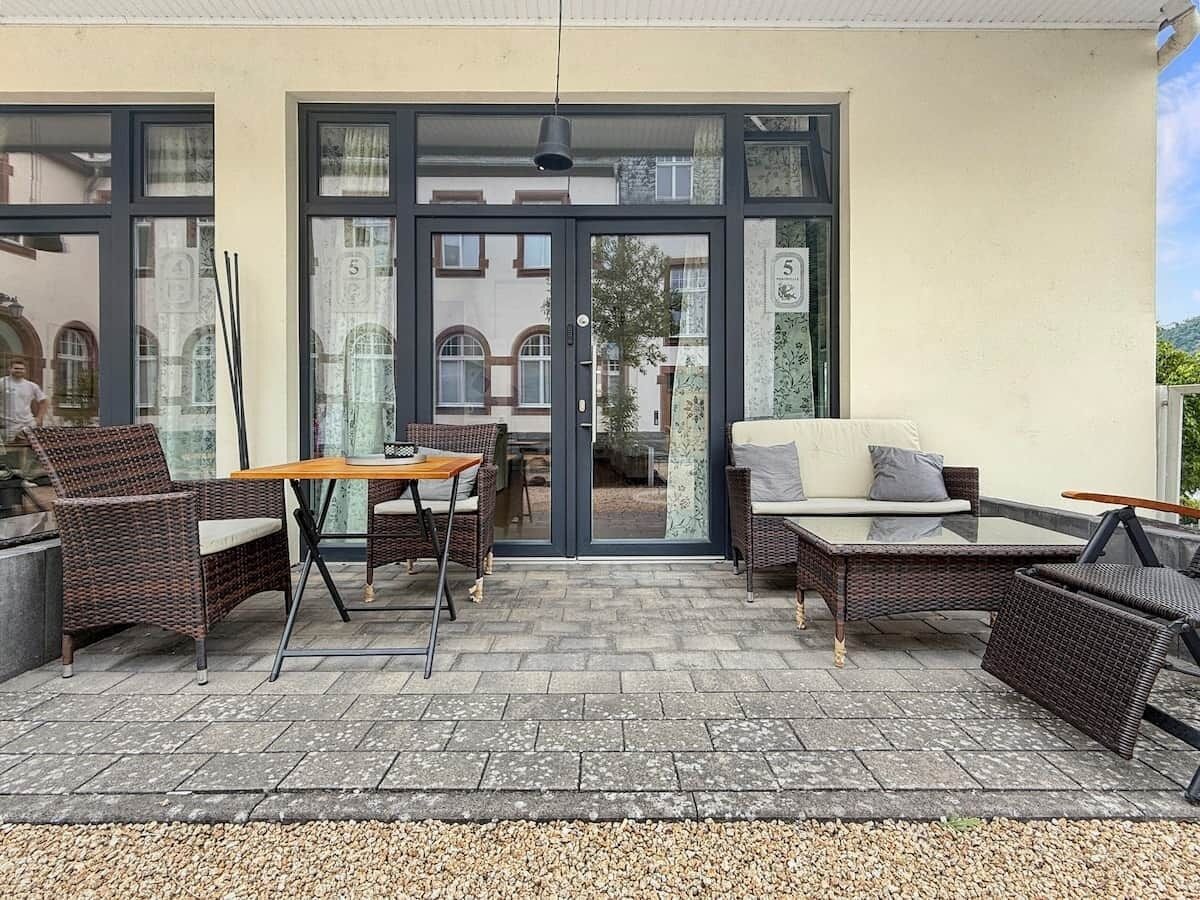 Un patio al aire libre con mobiliario de mimbre, una mesa de vidrio y un sofá.