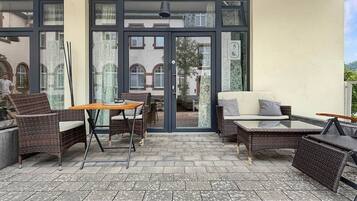 Un patio al aire libre con mobiliario de mimbre, una mesa de vidrio y un sofá.