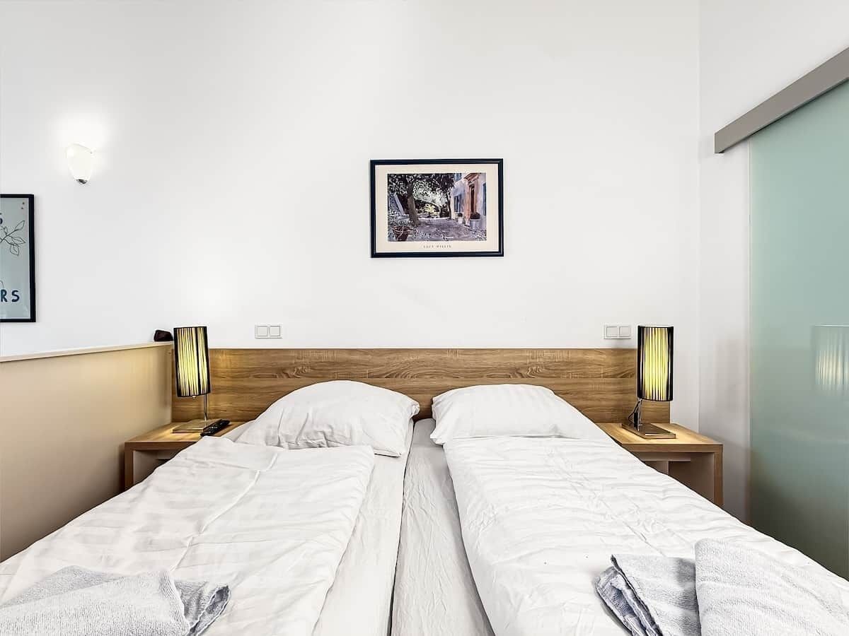 Una camera d'albergo con due letti, una testiera in legno, lampade sui comodini, un quadro appeso al muro e una porta scorrevole.