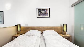 Una camera d'albergo con due letti, una testiera in legno, lampade sui comodini, un quadro appeso al muro e una porta scorrevole.