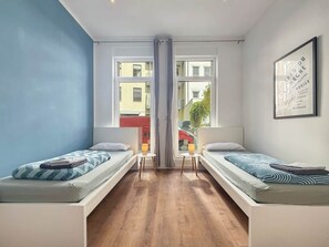 Una habitación con dos camas individuales, una mesita y una ventana que da a vistas de edificios.