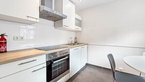A modern kitchen with white cabinets, a wooden countertop, a built-in oven, and a dining area with a round table and chairs. - Central & Cozy Loft Heart of Hannover Apartment (Hanover)