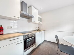 Eine moderne Küche mit weißen Schränken, einer Holzarbeitsplatte, einem Einbauofen und einem Essbereich mit rundem Tisch und Stühlen.