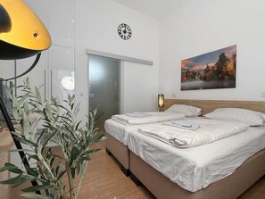 Moderni hotellihuone, jossa on sänky, kello, taulu ja ruukussa oleva kasvi.