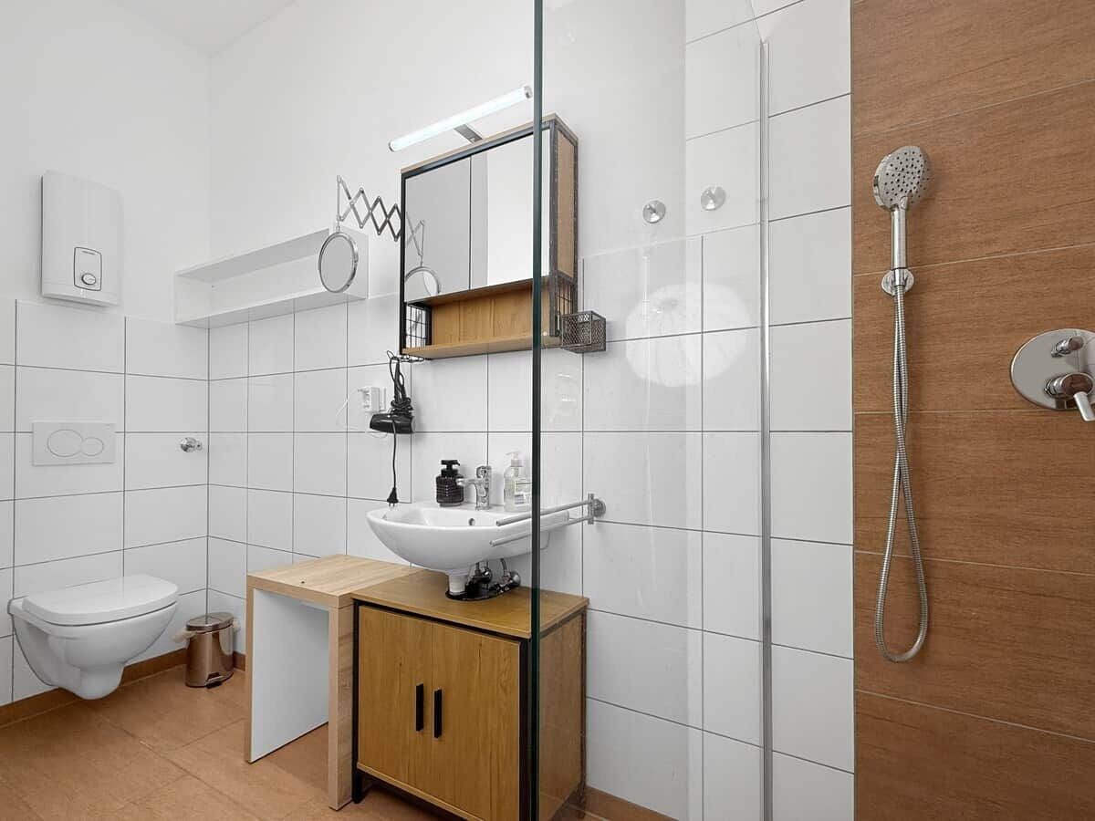 Ein modernes Badezimmer mit einem weißen Waschbecken, einem Holzkabinet und einer Dusche inklusive Handbrause.
