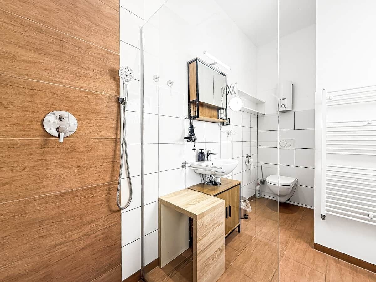 Een moderne badkamer met een houten wastafelmeubel, een glazen douchecabine en een wit toilet.