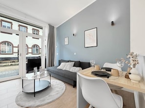 Een moderne woonkamer met een bank, een glazen salontafel, een eettafel met stoelen en uitzicht op een gebouw door een glazen deur.