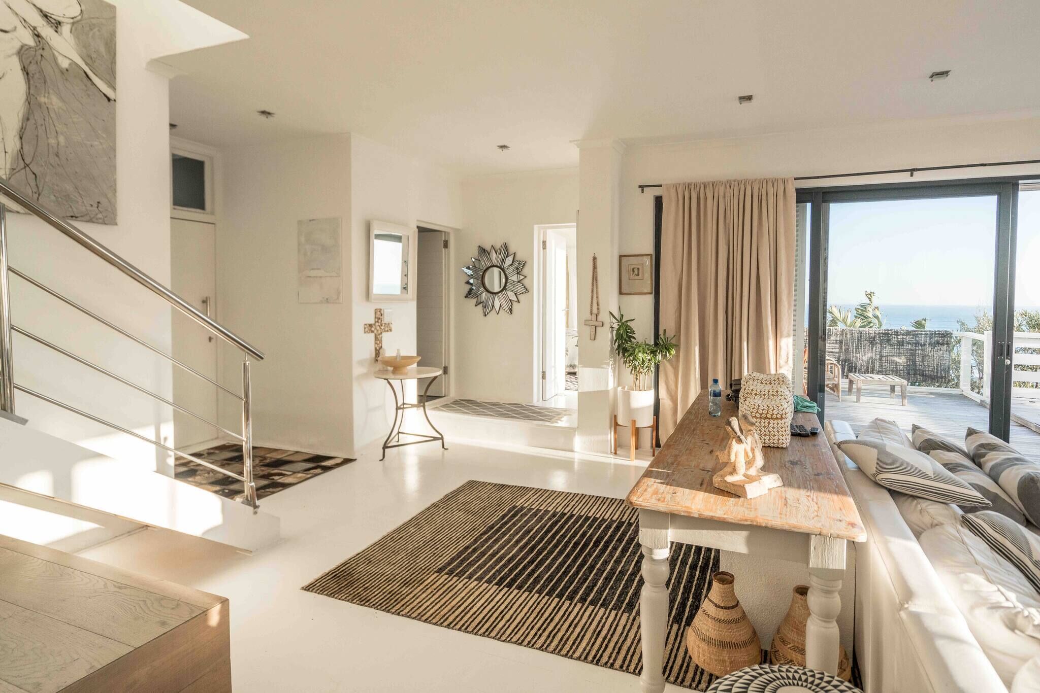 Un espace de vie moderne comprenant un escalier, une table à manger, un canapé et une grande fenêtre offrant une vue dégagée.