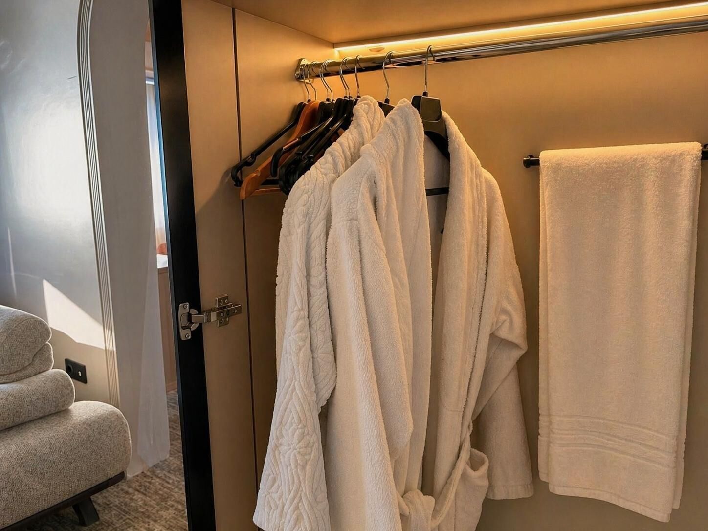 Un bagno con un portasciugamani pieno di diversi asciugamani bianchi, un accappatoio bianco e una sedia di legno.