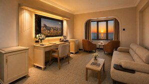 Habitación de hotel con escritorio, dos sillas, sofá, televisión y ventana con vista al atardecer.