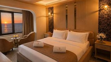A hotel room with a large bed, a desk, a chair, a small table with drinks, and a view of the sunset.