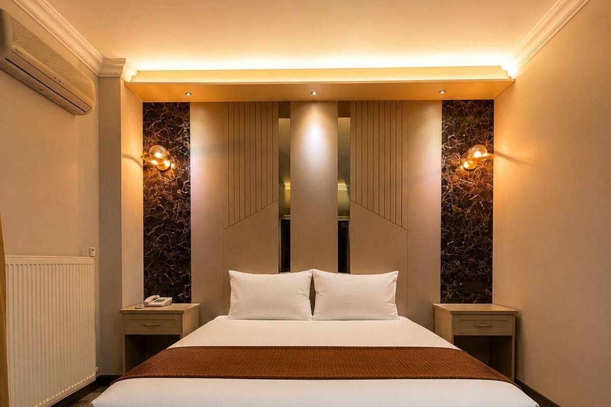 Habitación de hotel con una cama grande, dos mesitas de noche, aire acondicionado de pared y un radiador.