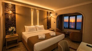 Habitación de hotel con cama, mesitas de noche, escritorio y vista al atardecer sobre el océano.