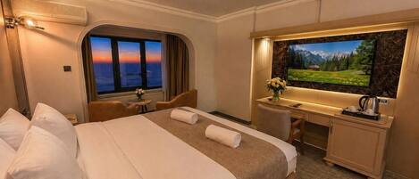 A hotel room with a bed, desk, chair, TV, and a window with a sunset view.