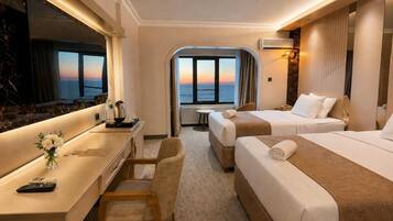 A hotel room with a desk, two beds, a view of the sea, and a large mirror.